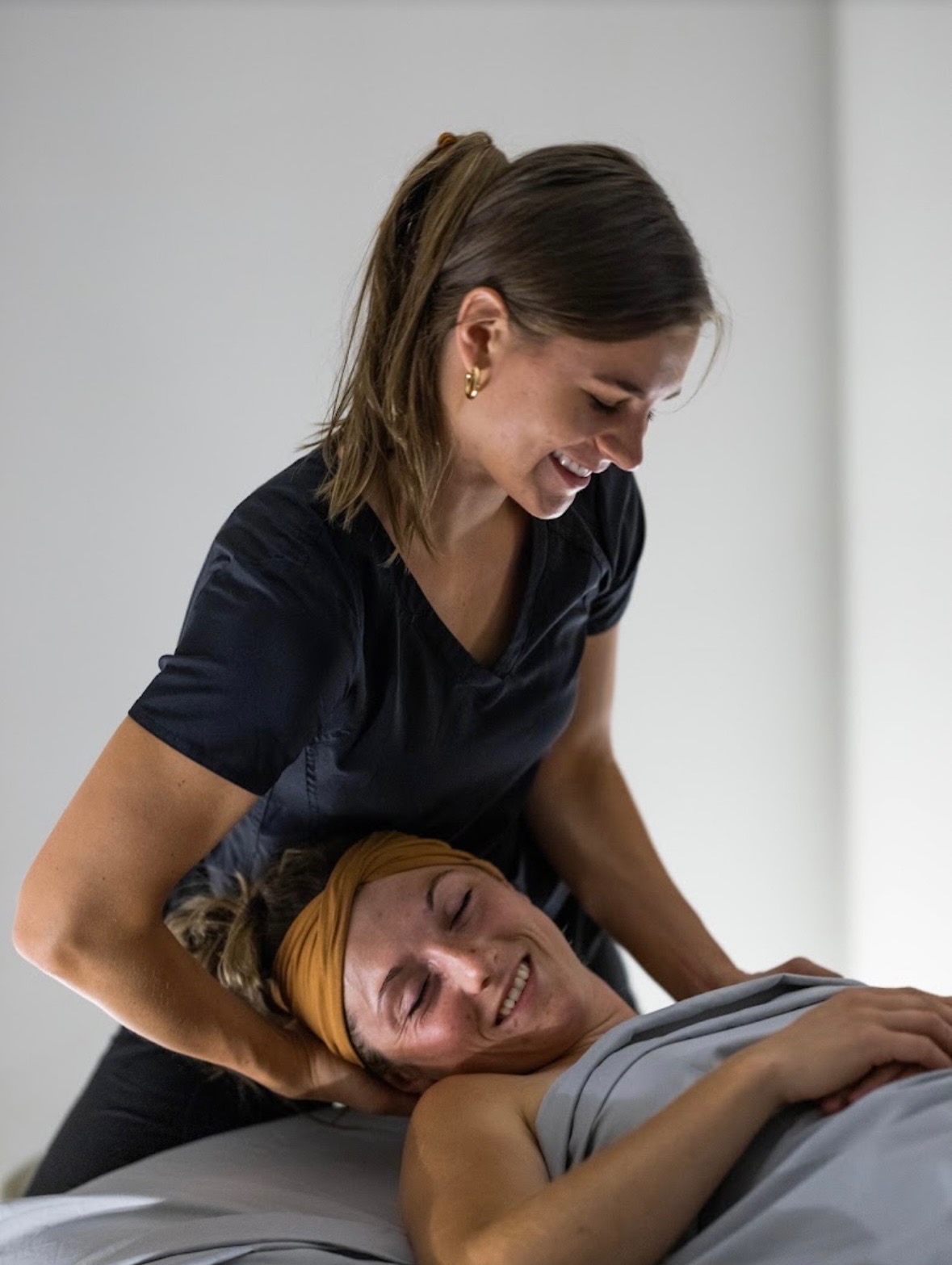 A manual therapist providing hands-on shoulder care to a client resting on a treatment table.